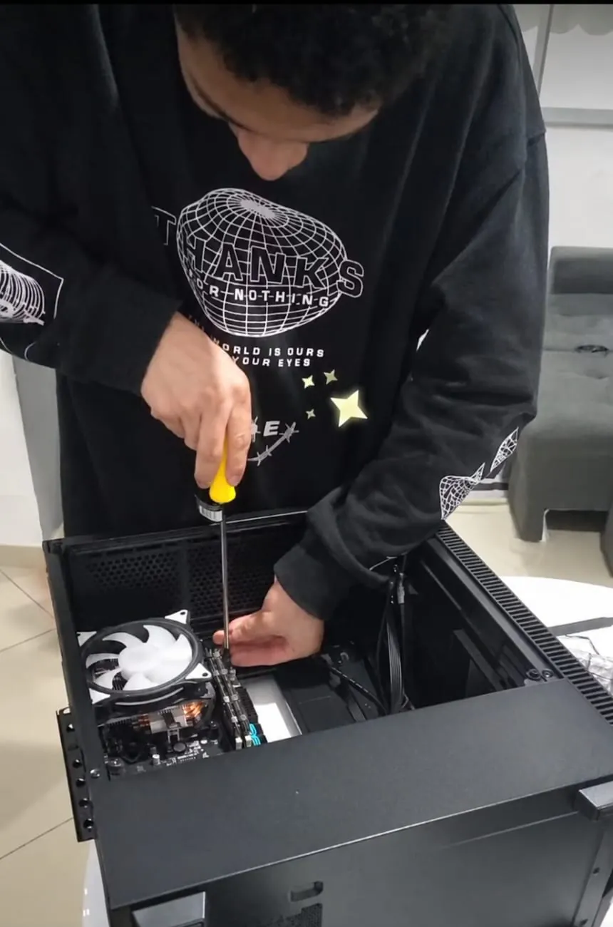 Carlos parafusando peças dentro do gabinete aberto, com o cooler e as memórias já instalados na placa-mãe.